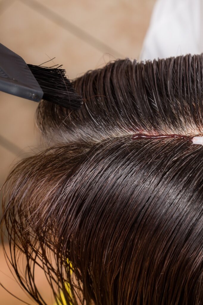 Hair dresser applying chemical hair color dye onto hair roots