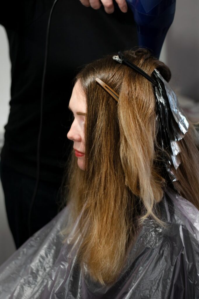 Hairdresser is making highlights for the young fair haired woman