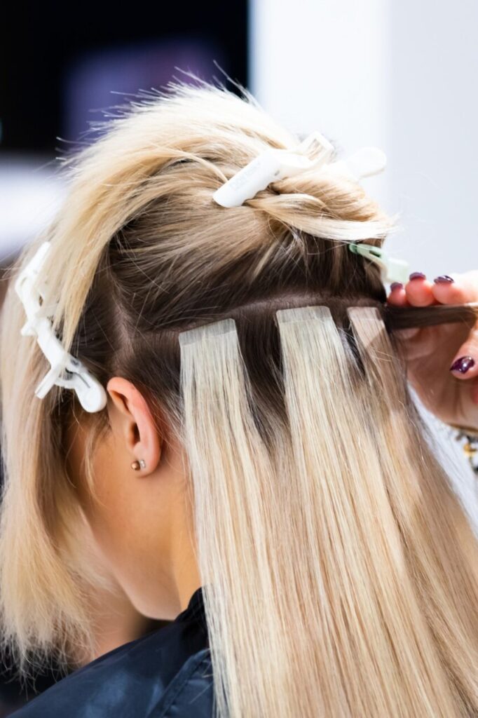 Professional hairdresser making hair extensions for blonde girl in a beauty salon